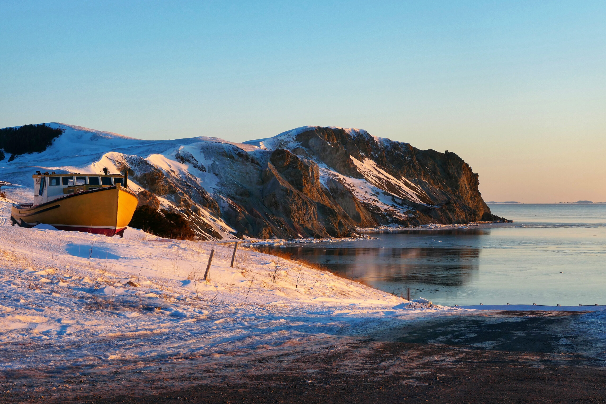 Un bateau posé sur la neige au bord d’une mer gelée aux Îles de la Madeleine, un paysage hivernal unique.