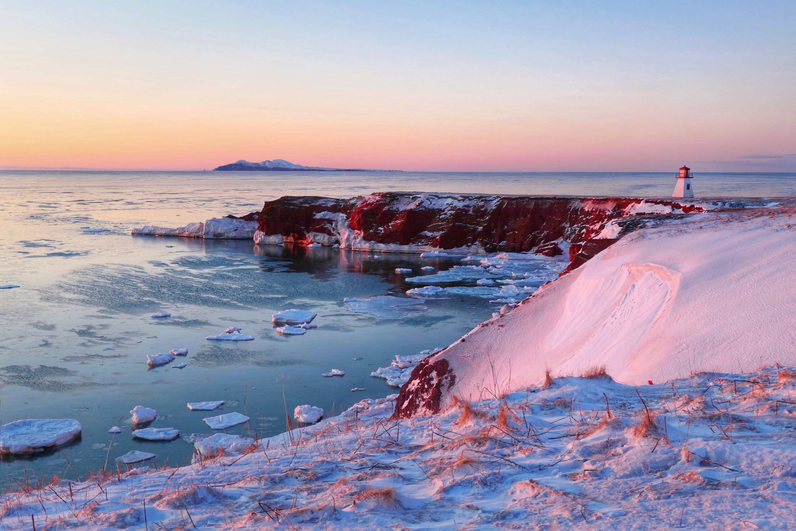 Lever de soleil hivernal sur la côte des Îles de la Madeleine avec un phare et mer gelée