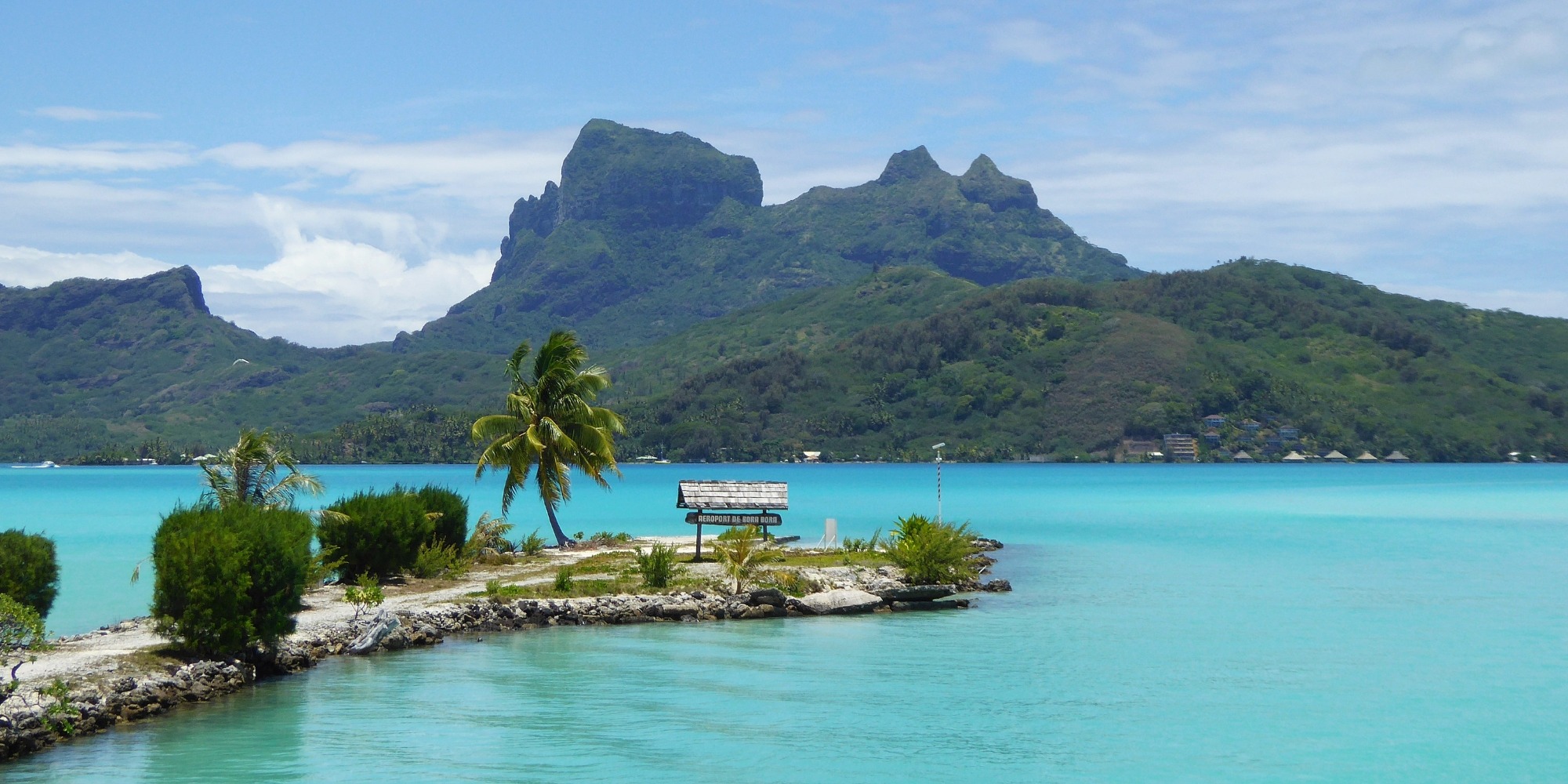 Panneau aéroport de Bora Bora sur le motu — lagon turquoise et mont Otemanu, Polynésie française Panneau "Aéroport de Bora Bora" sur le motu avec cocotier, lagon turquoise et mont Otemanu en arrière-plan, Polynésie française