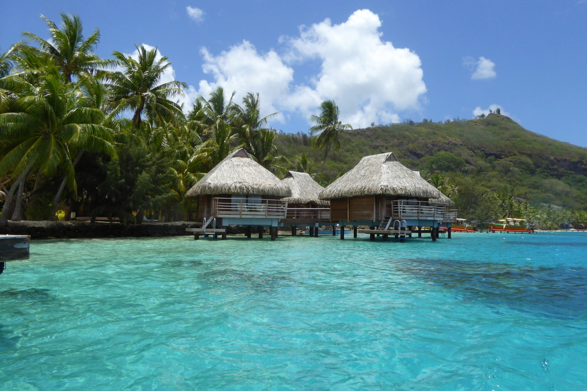 Bungalows sur pilotis au toit de chaume sur le lagon de Bora Bora — Polynésie française Deux bungalows sur pilotis au toit de chaume sur le lagon turquoise de Bora Bora avec une colline verdoyante en arrière-plan, Polynésie française
