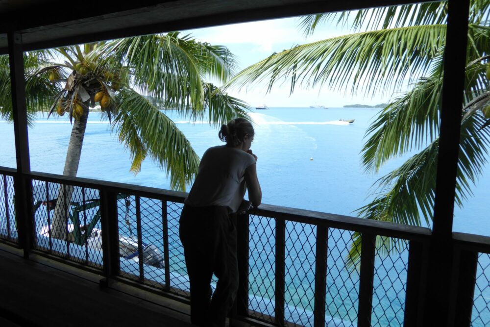 Silhouette accoudée au balcon du Sunset Hill Lodge contemplant le lagon bleu de Bora Bora encadré de cocotiers, Polynésie française
