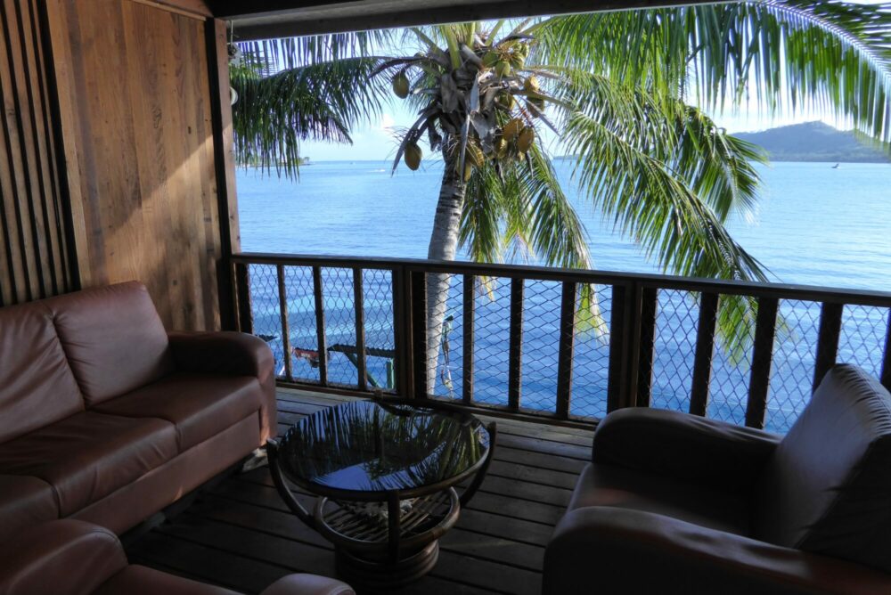 Terrasse du Sunset Hill Lodge à Bora Bora avec canapés en cuir, cocotier et vue panoramique sur le lagon bleu, Polynésie française