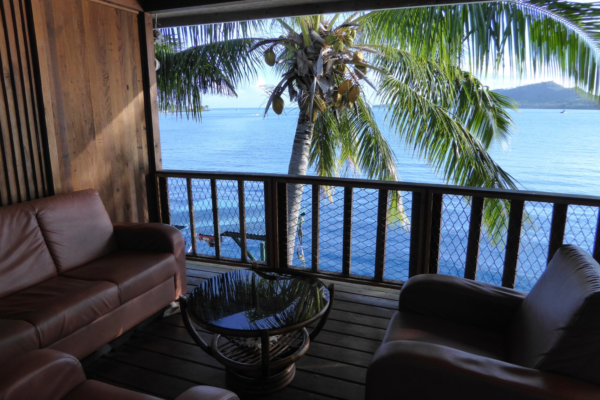 Terrasse du Sunset Hill Lodge à Bora Bora avec canapés en cuir, cocotier et vue panoramique sur le lagon bleu, Polynésie française