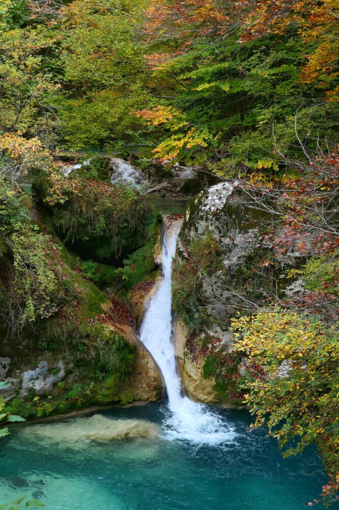 Cascade se jetant dans un bassin turquoise entouré de feuillages d'automne