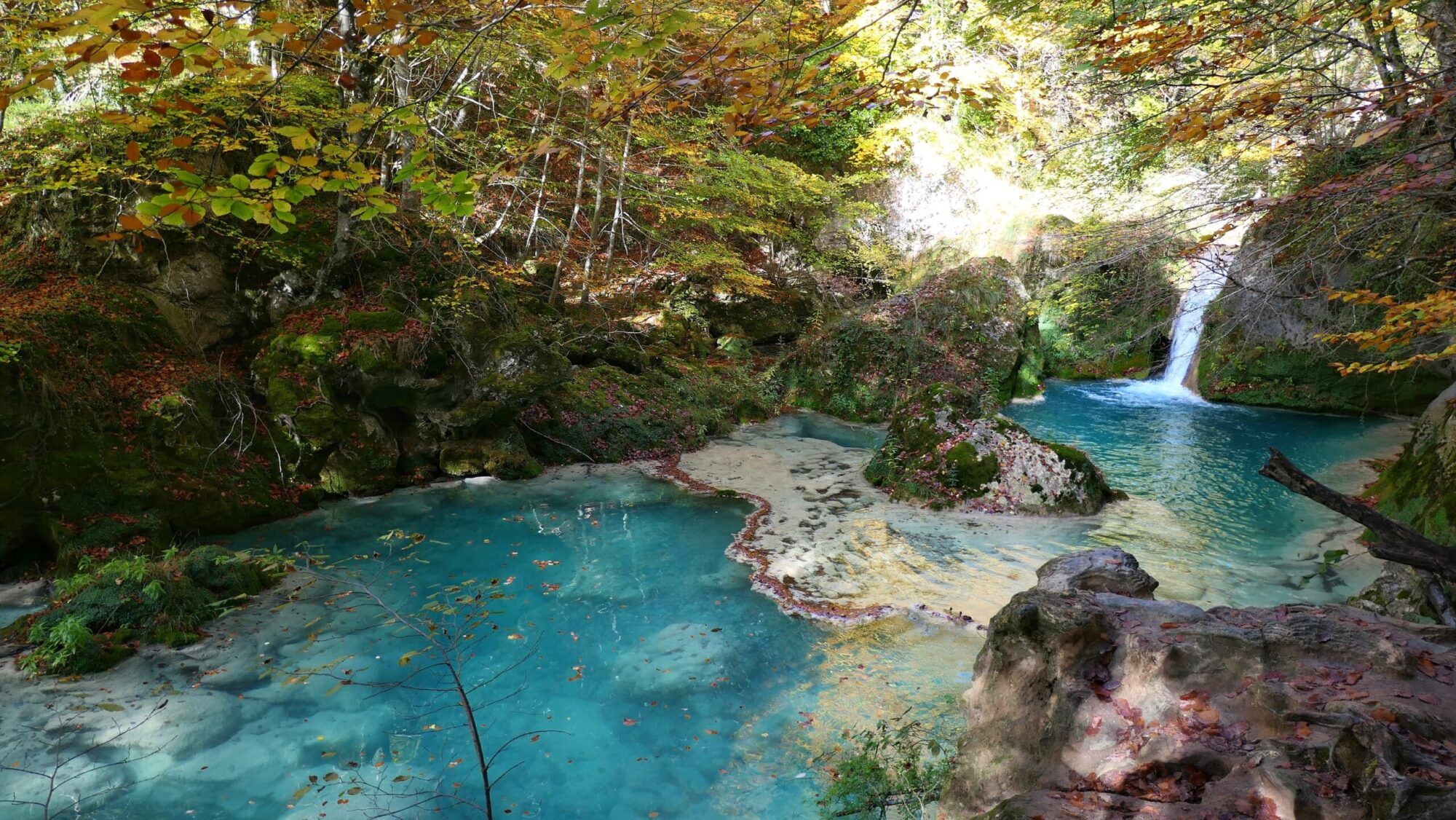 Cascade et bassins turquoise d'Urederra Cascade se déversant dans des bassins d'eau turquoise entourés de rochers moussus à Urederra